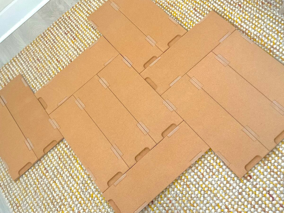 12 TALAYA Solid Ground tiles arranged cork-side up in an asymmetrical star-like configuration on a patterned yellow, white, and orange rug, overhead view, natural light